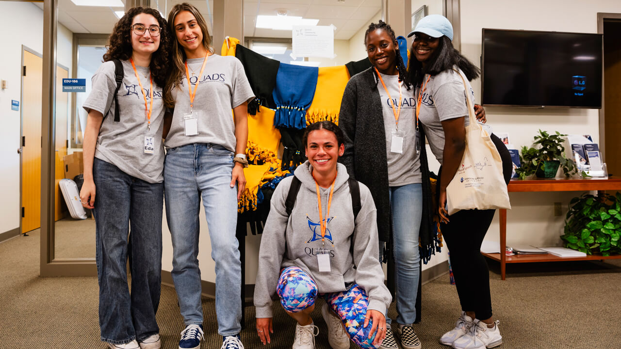 Quinnipiac students stand in front of hand-made scarves made by QUADS students to give back to their communities.