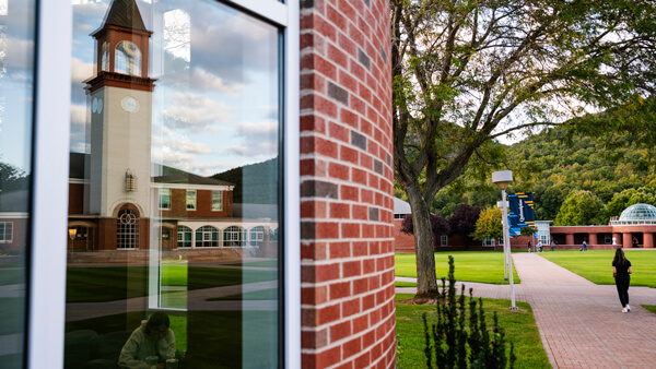 The library clocktower reflects on the student center windows as a student walks across the quad