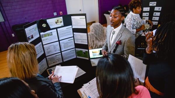 An entrepreneur presents a poster board with his business plan to people who are listening