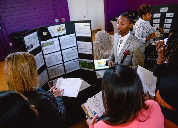 An entrepreneur presents a poster board with his business plan to people who are listening