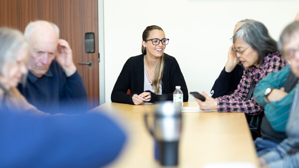 Amanda Panniello sits at a table talking to a group of older adults.