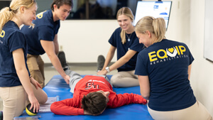 Four physical therapy students talk with a patient lying on an exam table