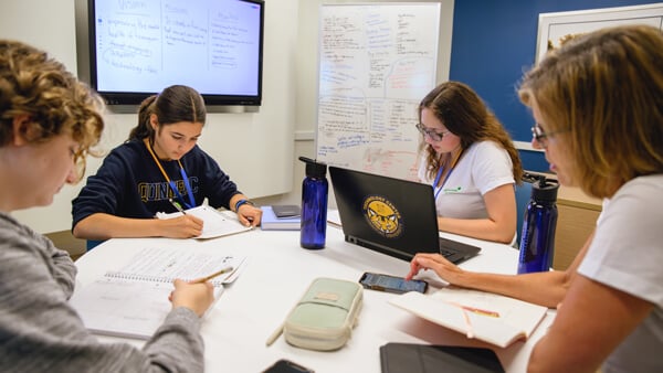 Girl Scouts and students collaborate at a table with laptops and white boards