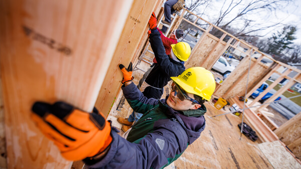 Quinnipiac students wear hard hats and build an outdoor structure on a cool, clear day