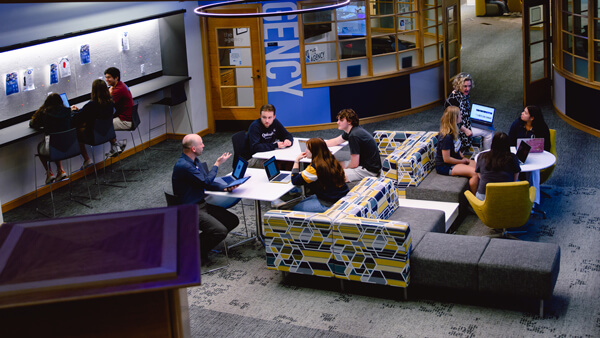 Students and professors sit on colorful couches and work at laptops in The Agency space