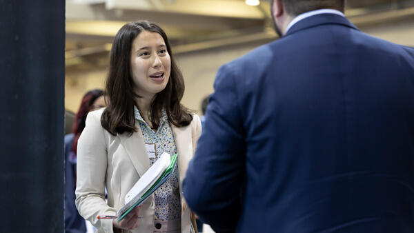 A student and a business owner in suits talk with each other at a Quinnipiac career fair