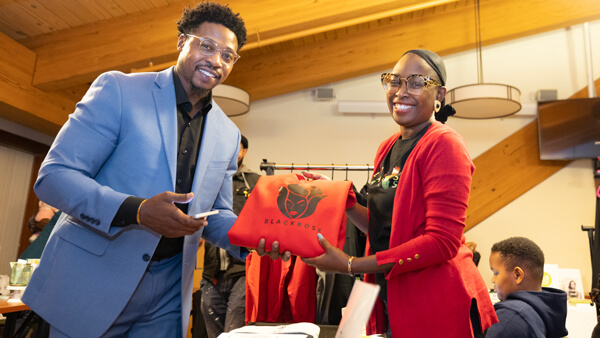 Two small business owners smile and pose with their product in a Quinnipiac room