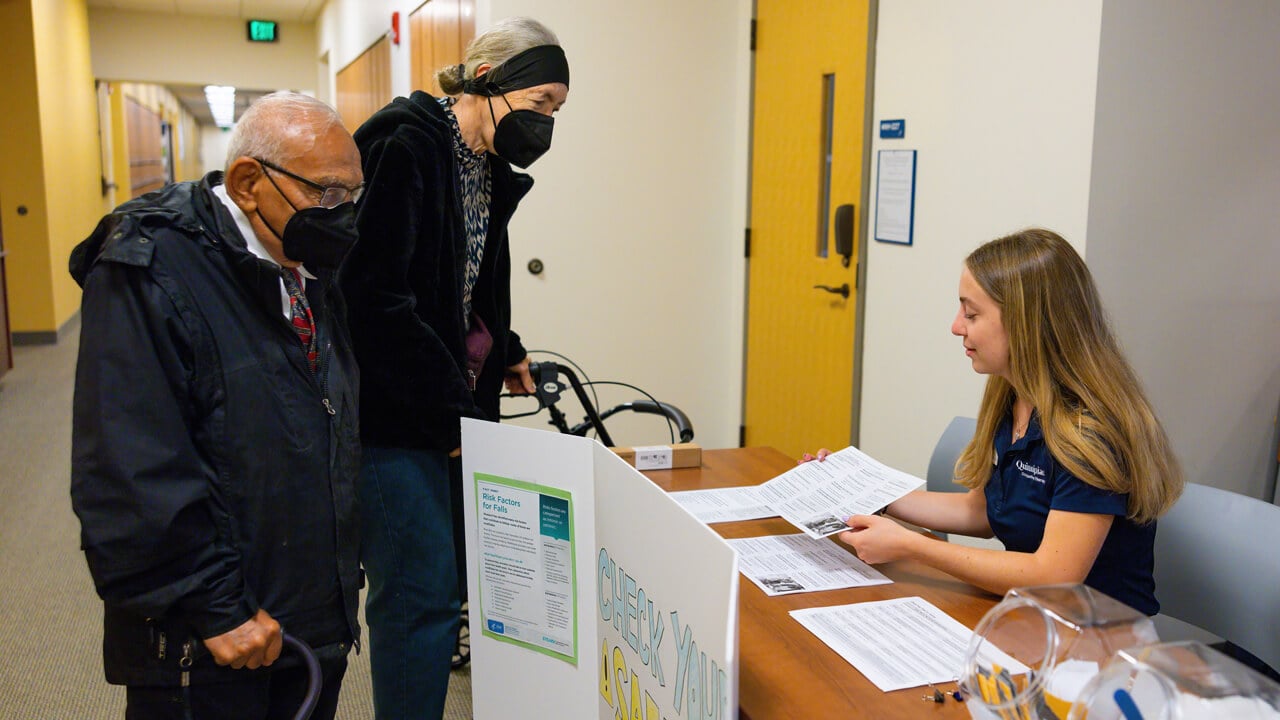 Two older adults speak with a physical therapy student at a fall prevention event