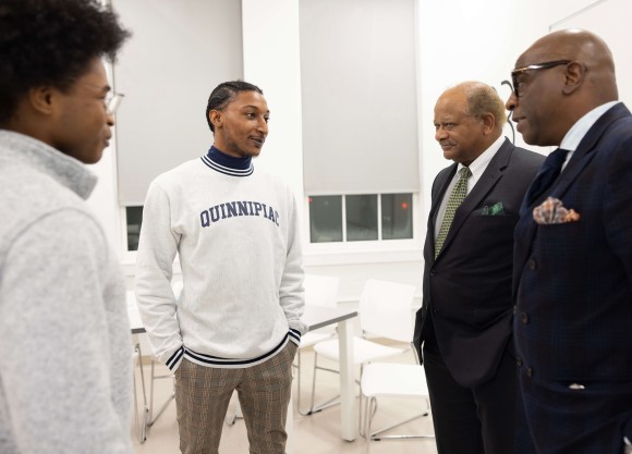 Four men speak in a classroom