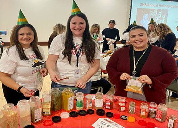 Three individuals pose while volunteering at a soup station
